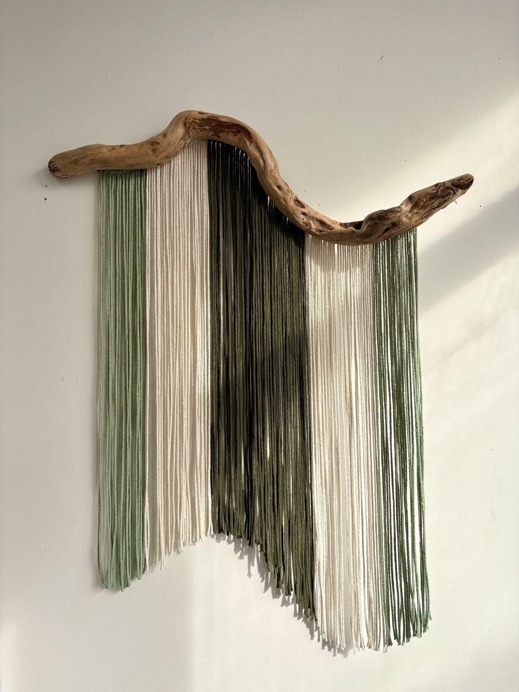 Fiber wall hanging in a green ombre, mounted on driftwood