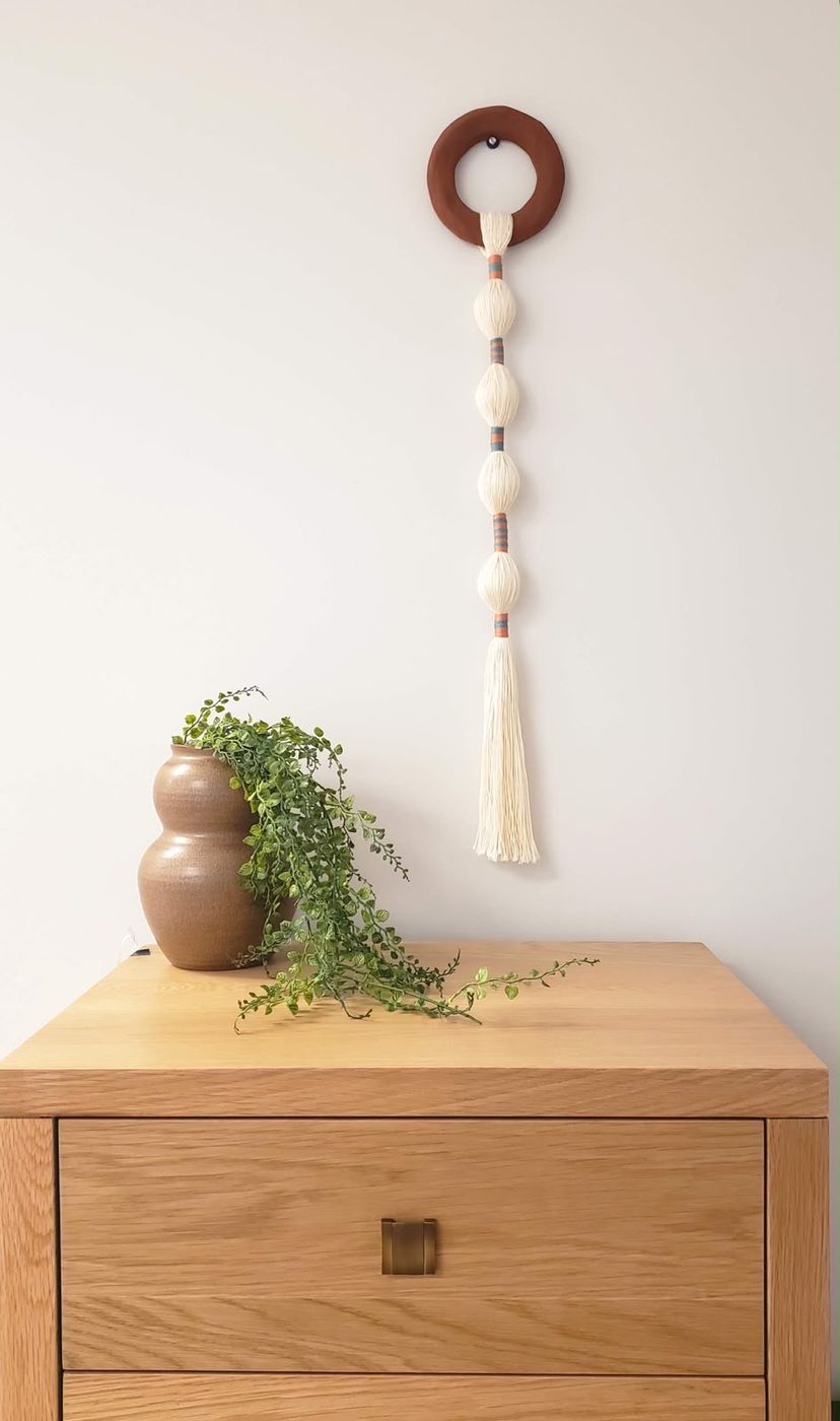 Wall hanging with a rust wooden ring and cream tassel, on a dresser