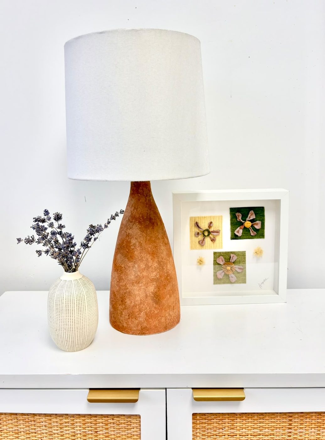 Tall terracotta lamp styled on a dresser with framed pieces