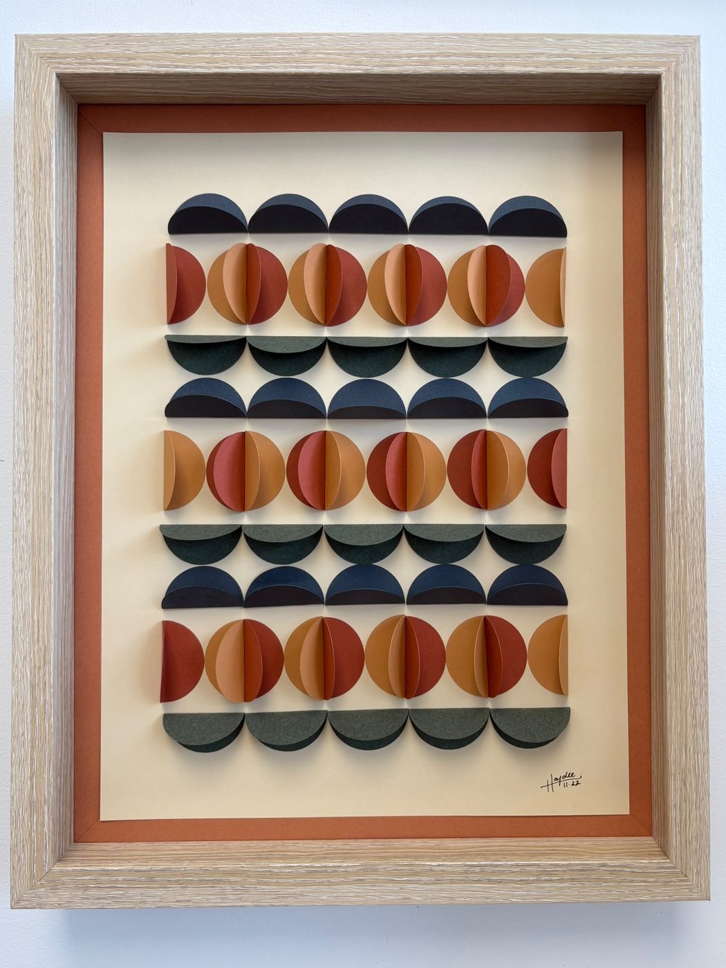Framed scalloped paper piece in rows of navy, rust and cream