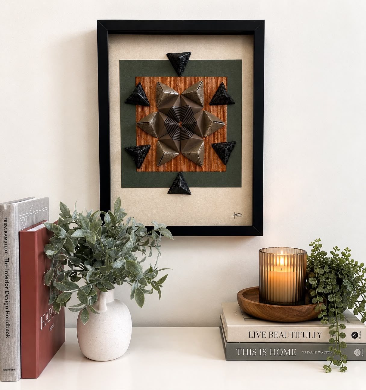 Framed origami star wall piece in bronze and black, styled on a shelf