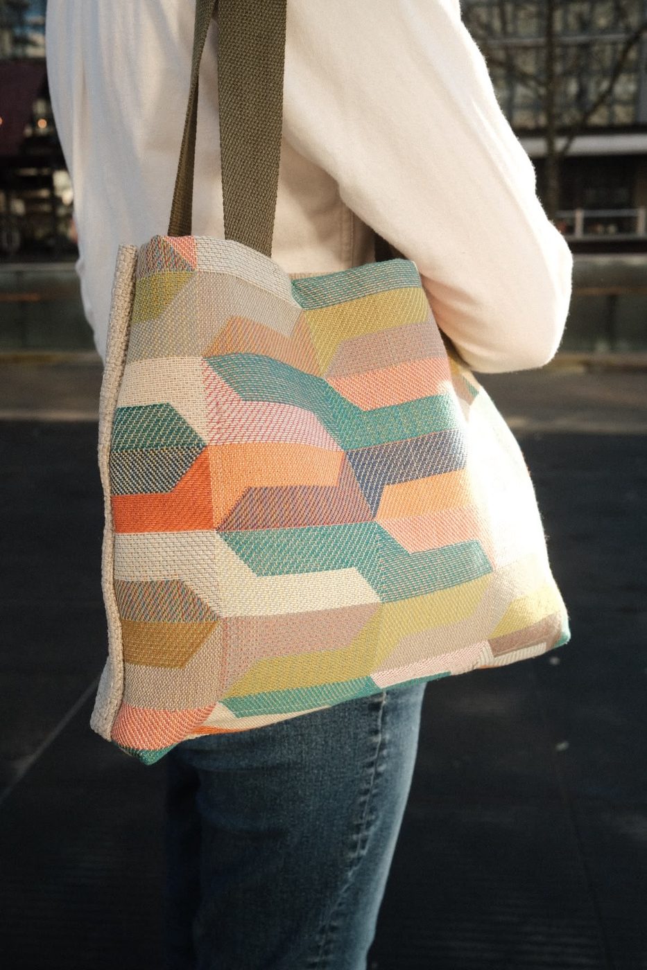 Detail of a woven geometric tote in teal, coral and orange