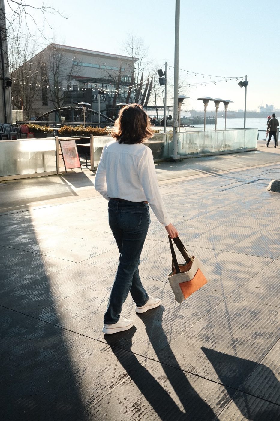 Woman walking with a linen tote with an orange pocket, on the waterfront
