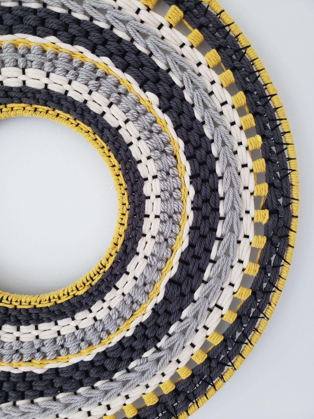 Woven circular wall piece in navy, yellow and grey